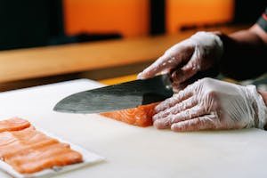 Chef slicing fresh salmon with precision using fillet knife for sushi preparation in a vibrant kitchen setting.